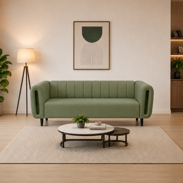 A modern sage green velvet loveseat sofa with vertical channel tufting and integrated side armrests, styled in a minimalist living room with a beige rug, round coffee tables, a floor lamp, and abstract wall art.